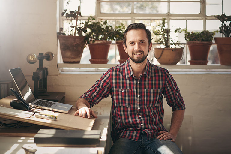 Man sitting down in his home office next to his laptop smiling